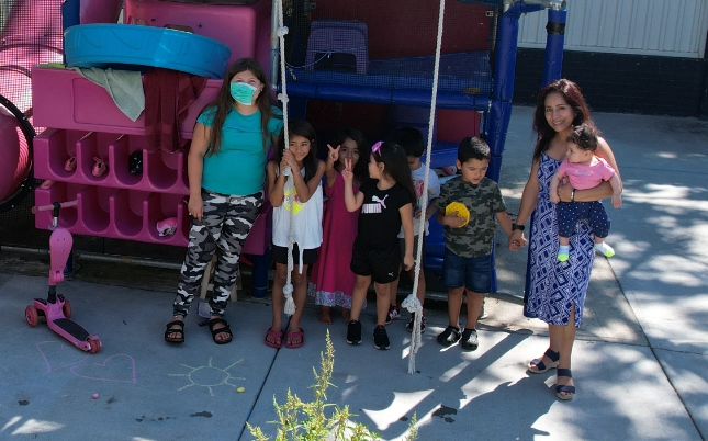  Daycare provider with a group of children standing outside in front of a playground