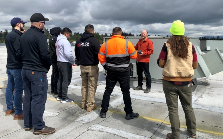 Group of people standing on rooftop listening to a contractor explain technology