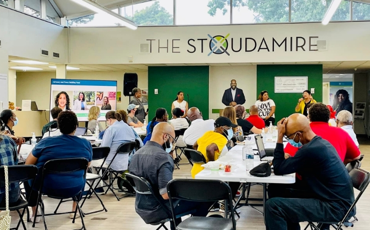 Event space with people sitting in tables and chairs, sign on the wall says “The Stoudamire”