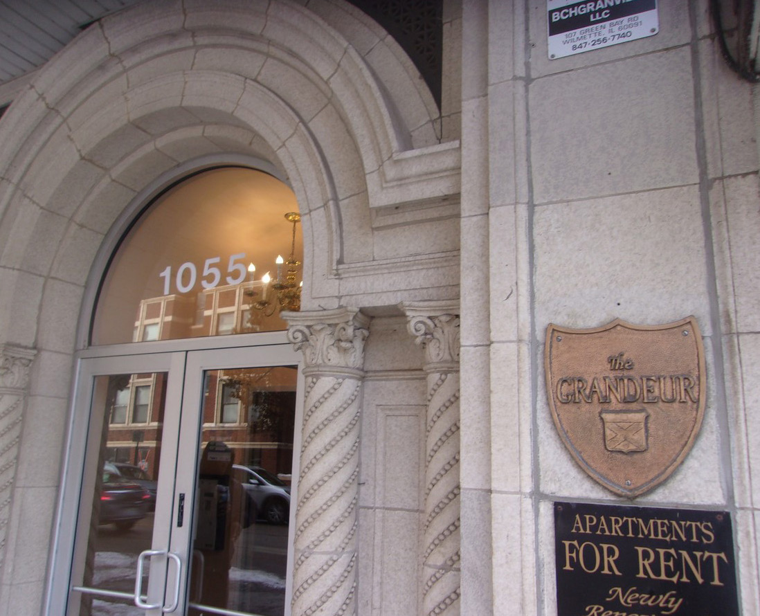 Image of archway entrance to large grey multifamily building.