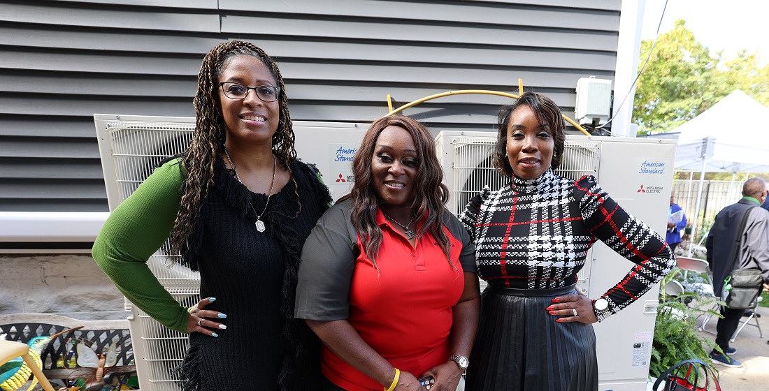 Three women standing in front of heating equipment smiling at the camera