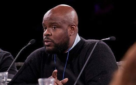 Man speaking into microphone sitting at a table