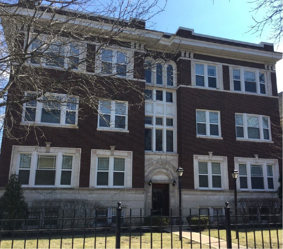 Exterior of a large multifamily building with red brick and white windows.