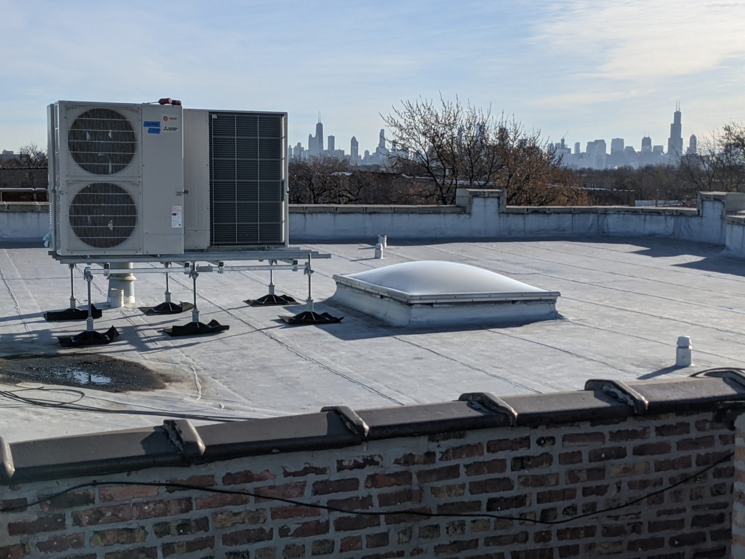 Rooftop of a building with an outdoor heat pump unit installed. In the background you can see the skyline of Chicago. 