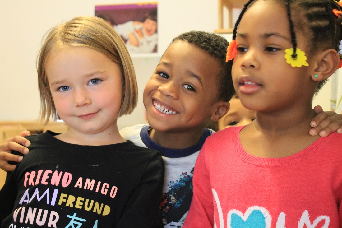 Three children in a classroom smiling at the camera