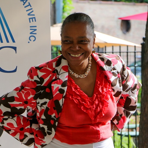 Image of Black woman smiling outdoors wearing a colorful jacket.