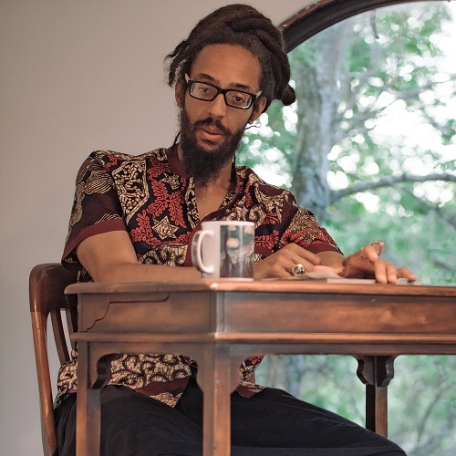 Image of Black man sitting at a desk in front of a large window.